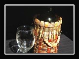 X001.  Finished wine bottle holder made of split cedar bark, with clay bead embellishments. 